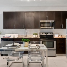 Sleek kitchens. Spacious layouts.  a kitchen with dark cabinets and a dining table